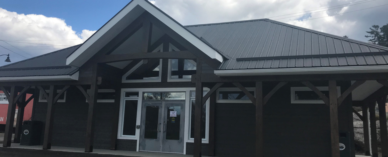 Close up image of the Welcome Centre. Shows wooden beams, peaked roof, blue wooden siding.